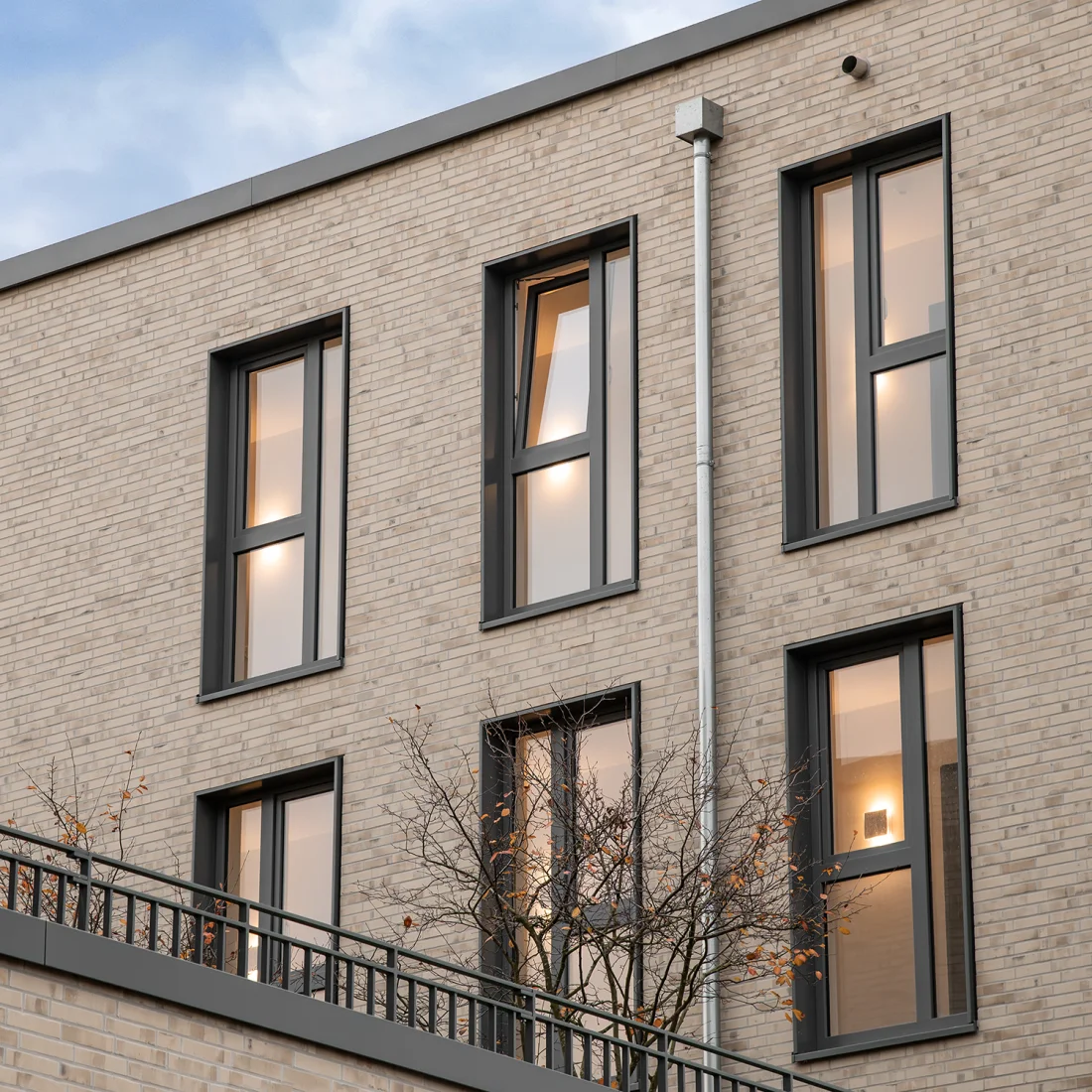 Das Bild zeigt ein verklinkertes Gebäude, bei dem das COVER-System von Abel für die Laibungs- und Bekleidungszargen verwendet wurde. Die Zargen tragen mit ihrem warmen Grauton zum harmonischen Gesamtbild des Gebäudes bei und schützen gleichzeitig vor Witterungseinflüssen.