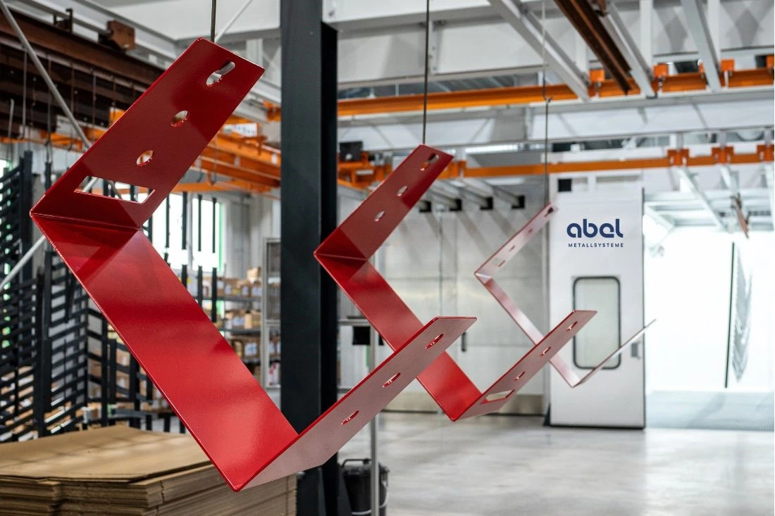 Rote, pulverbeschichtete Metallteile hängen in einer modernen Pulverbeschichtungsanlage bei Abel Metallsysteme.